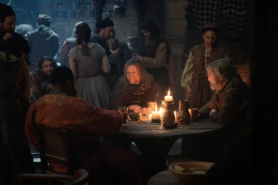 Ulf White junto a Hugh Hammer sentados en una mesa iluminada con velas en una taberna - House of the Dragon 3x04